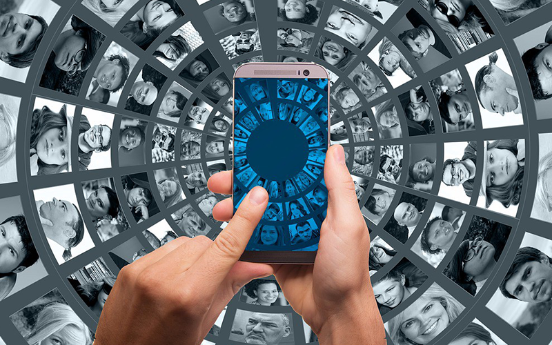 Person using a mobile phone with faces of many people encircling their hands